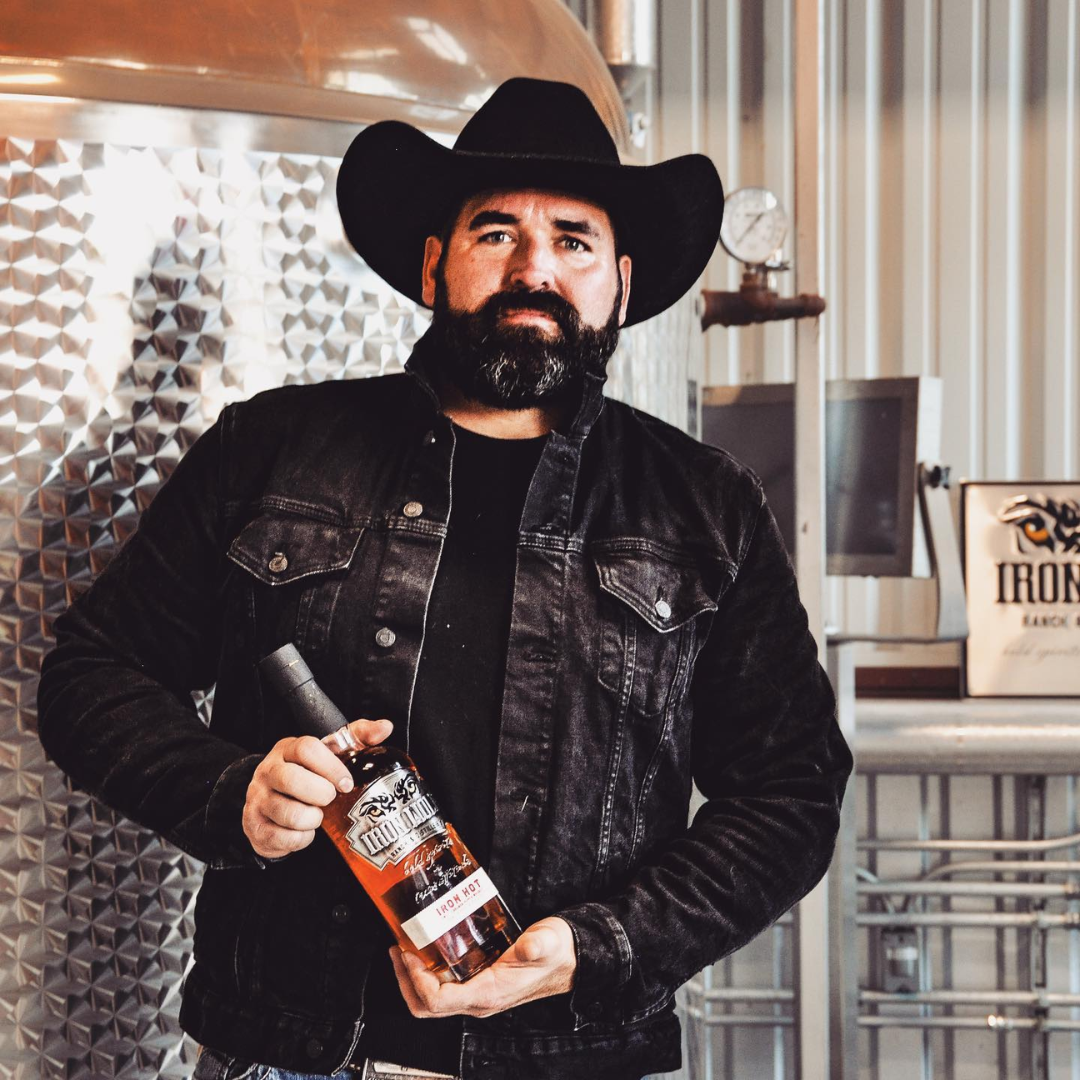 Singer Denny Herrin in the Iron Wolf Distillery still house holding a bottle of whiskey